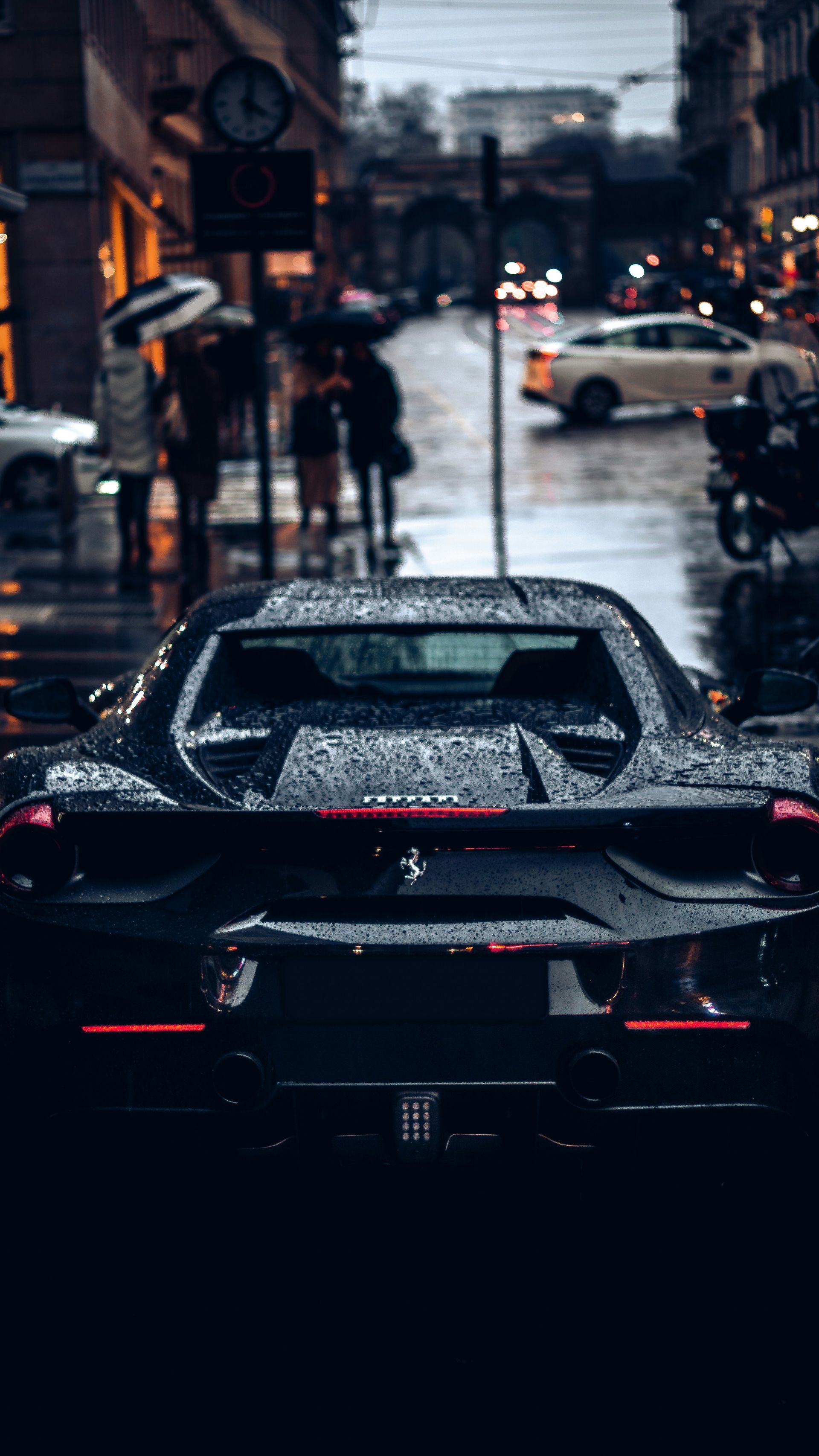 A black Ferrari sports car covered in raindrops on a wet city street
